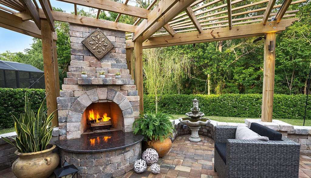 Elegant outdoor pool, bubbling spa, and stone fireplace lit at night
