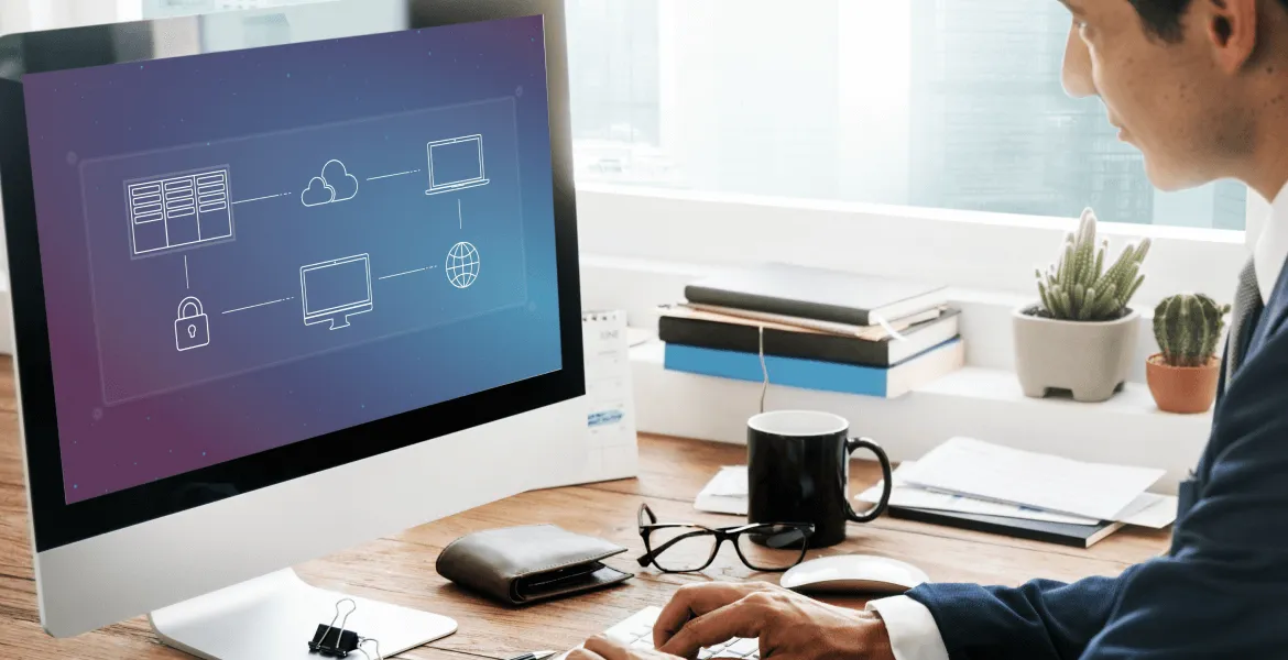 Man working at a desk with a computer displaying a cloud network diagram