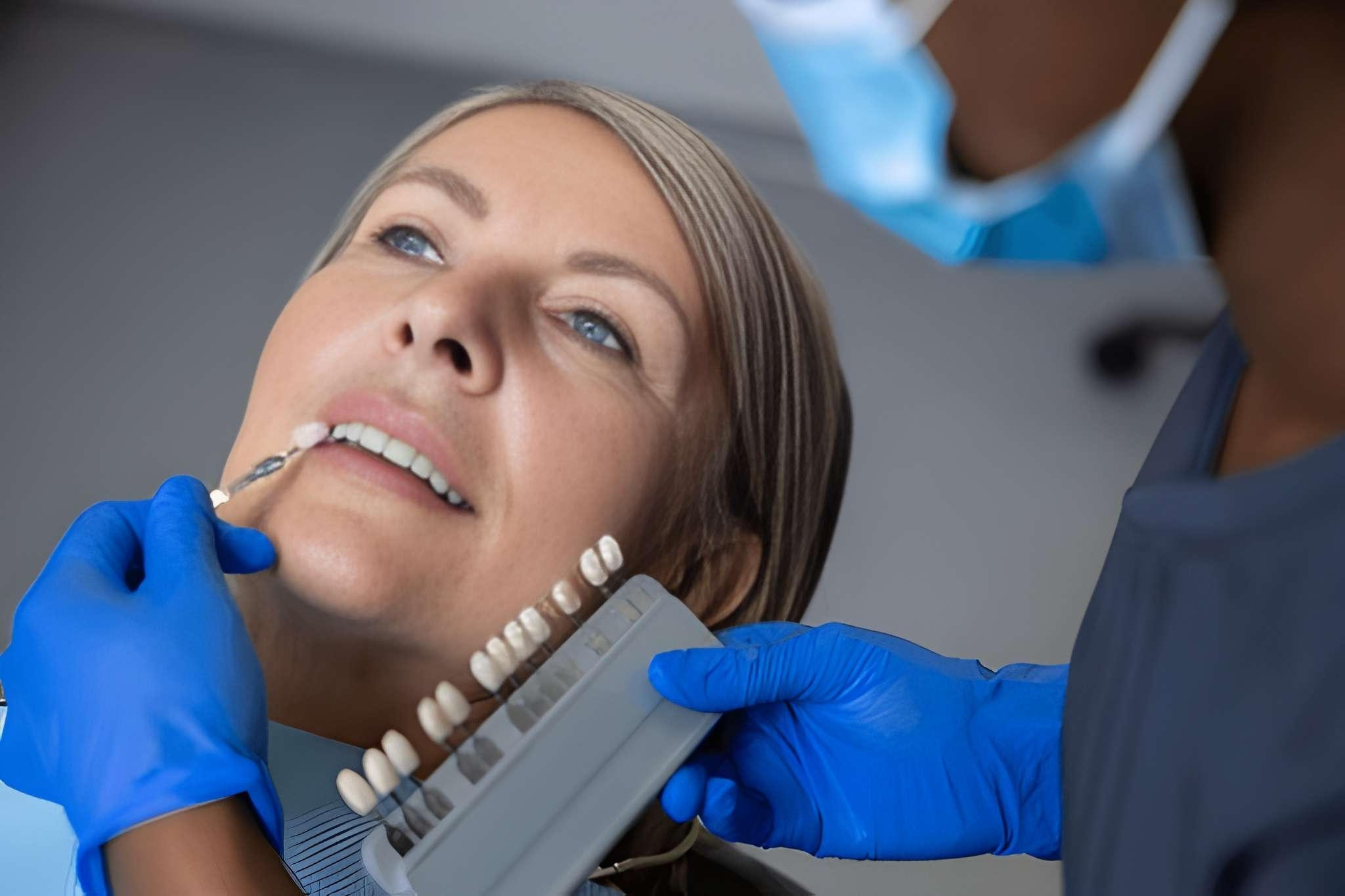 A patient smiling in a dental office while being shown dental shade samples for porcelain veneers.