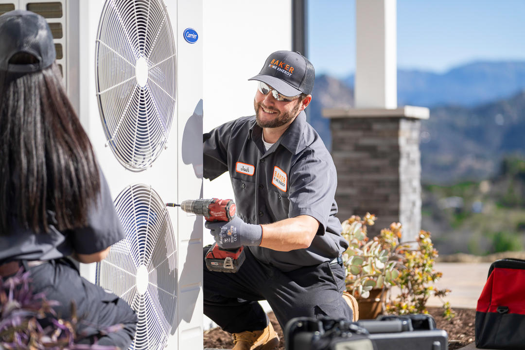 Baker Home Services technician standing outside a home near AC units